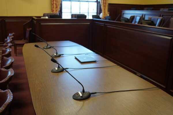 Microphones on table in front of chairs for a committee hearing.