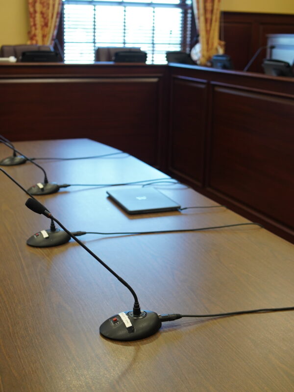 Microphones on table in front of chairs for a committee hearing.