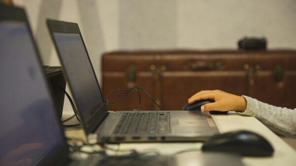 Kid's hand on a mouse in front of a laptop computer.