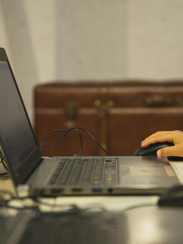 Kid's hand on a mouse in front of a laptop computer.