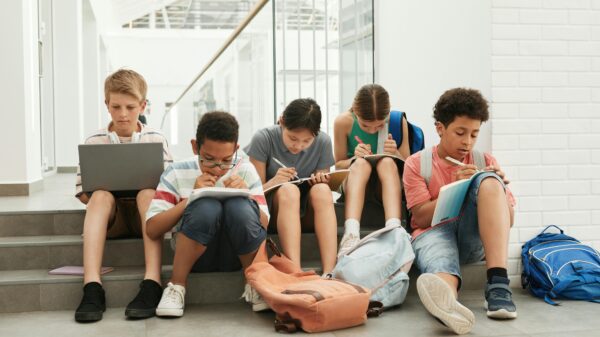 Kids doing homework sitting in a line with book and laptops.