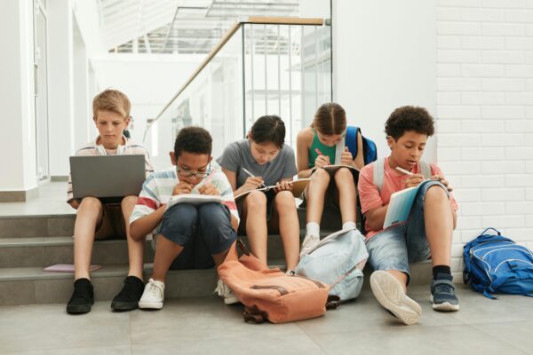 Kids doing homework sitting in a line with book and laptops.