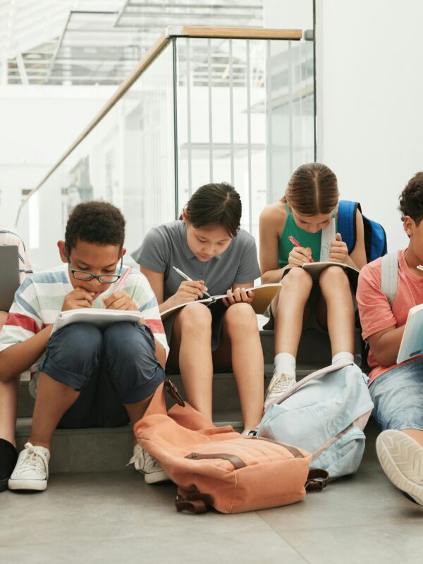 Kids doing homework sitting in a line with book and laptops.