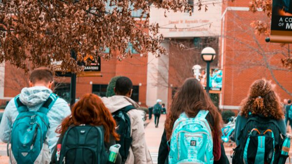 Photo of students walking into a school wearing sweatshirts and backpacks.