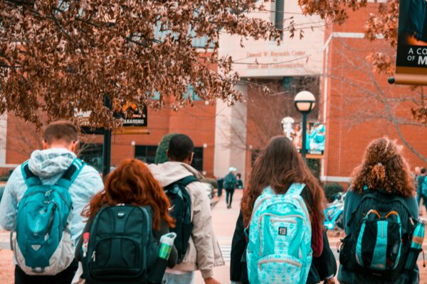Photo of students walking into a school wearing sweatshirts and backpacks.