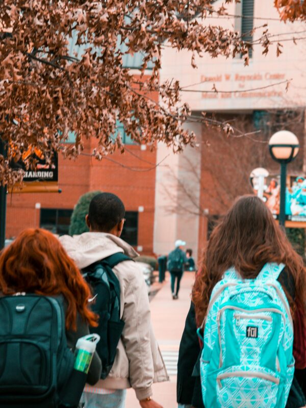 Photo of students walking into a school wearing sweatshirts and backpacks.