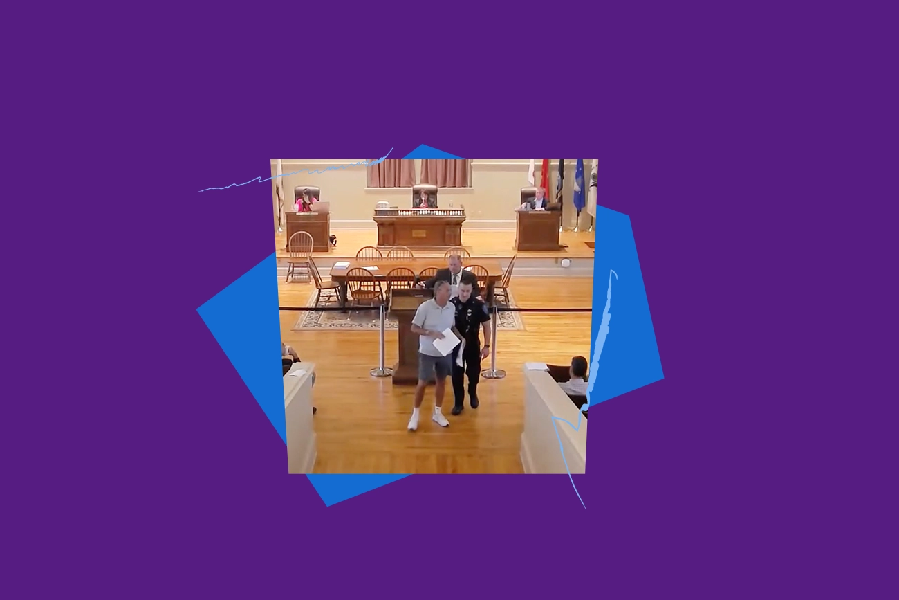 Robert Cote being led out of a Warwick Town Council meeting by a police officer, with purple and blue shapes and squiggles framing the image.