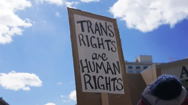 Protest sign against a blue sky with clouds that says "trans rights are human rights."