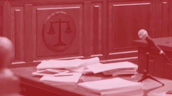 Dark red and pink image of a court room with a microphone and table with papers on it.