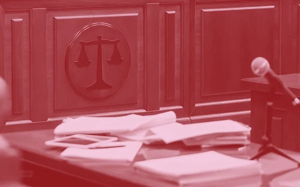 Dark red and pink image of a court room with a microphone and table with papers on it.